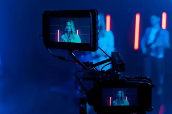 A performer in front of a camera and coloured lights on a music video set